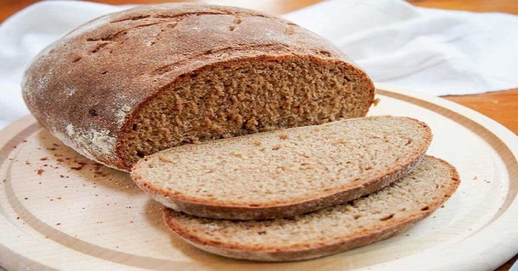 A picture of fresh and delicious barley bread on a wooden table, showing the bread with its golden color and distinctive texture. Barley bread is a healthy option rich in fiber and nutrients, ideal for those looking to supplement their diet with natural and nutritious options. The image is decorated with some whole barley grains and natural plants to highlight the authenticity and purity of the barley bread ingredients.